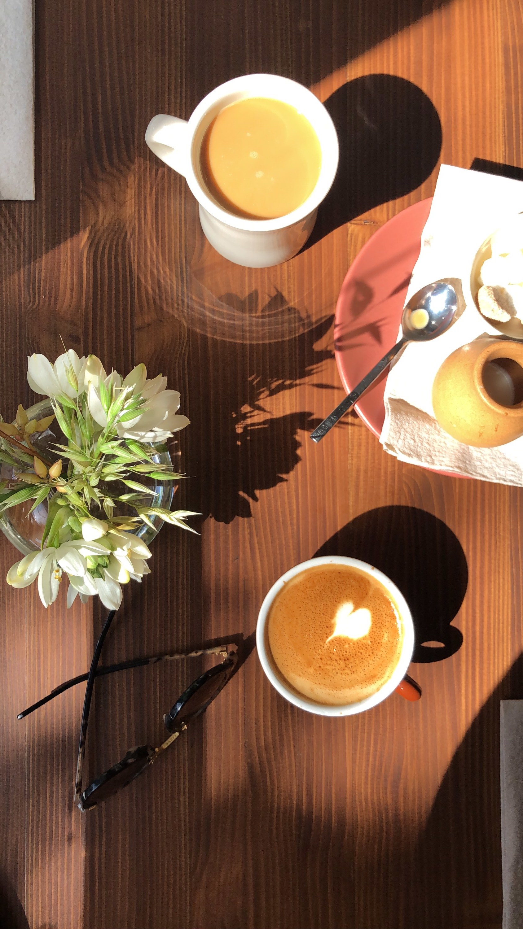 A cortado and a mug of coffee in morning light on a wooden table at Little Spoon